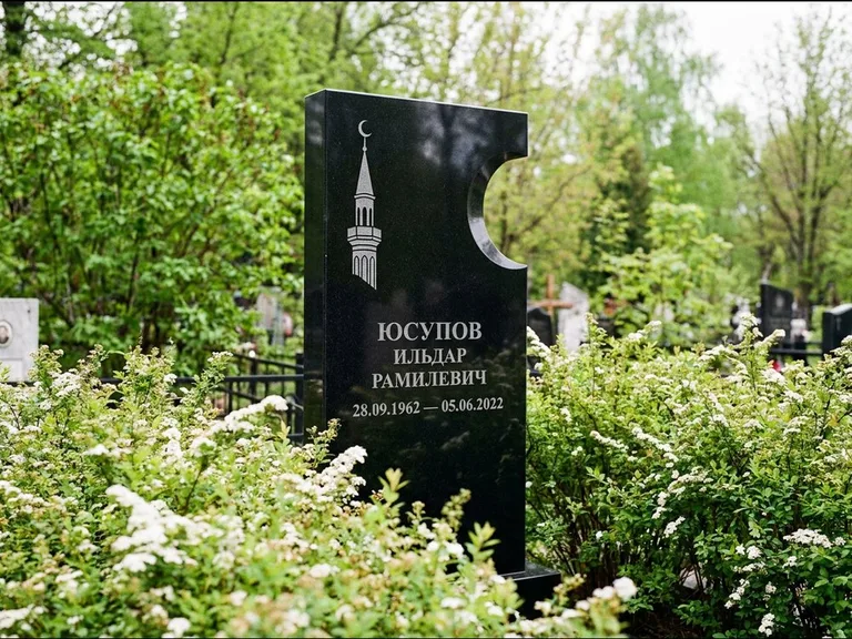 Мусульманский памятник с гравировкой мечети: стела с боковым вырезом в форме полумесяца — гравировка минарета с полумесяцем, низкие кусты спиреи в цвету, работа «Юсупов» в Сочи
